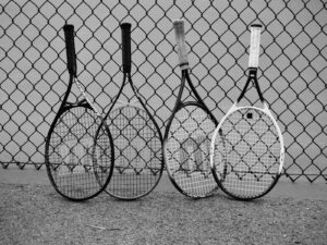 Four tennis rackets lean against a fence.