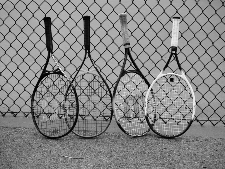 Four tennis rackets lean against a fence.